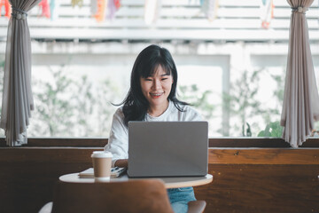 Fototapeta premium Business freelance concept, An engaging woman smiles warmly while working on a laptop in a bright and airy cafe, with a coffee cup at her side.