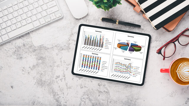 A digital tablet displaying colorful business analytics graphs alongside a keyboard, pen, glasses, and a cup of latte art coffee on a marble surface.
