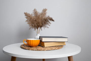  Cup and books on the table next to a vase on a white background. Minimalism 