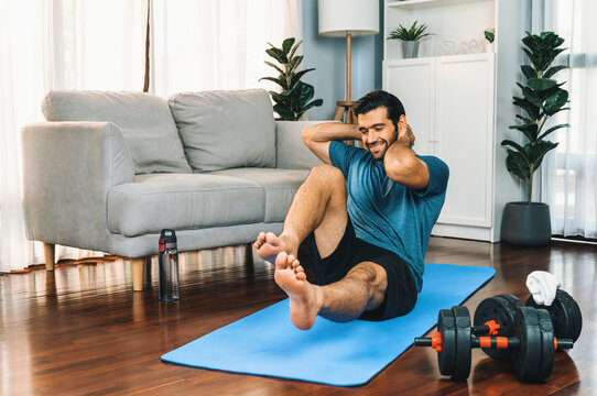 Athletic and sporty man doing crunch on fitness mat during home body workout exercise session for fit physique and healthy sport lifestyle at home. Gaiety home exercise workout training concept.