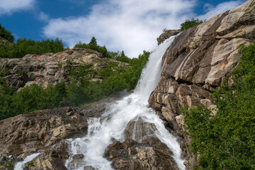 Obraz premium View of the Alibek waterfall formed by the fall of the Jalovchatka River from the Alibek glacier on a sunny summer day, Dombay, Karachay-Cherkessia, Russia
