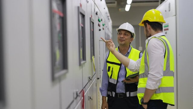 Professional electrical engineer in safety uniform working at factory server electric control panel room. Industrial technician worker maintenance checking power system at manufacturing plant room.