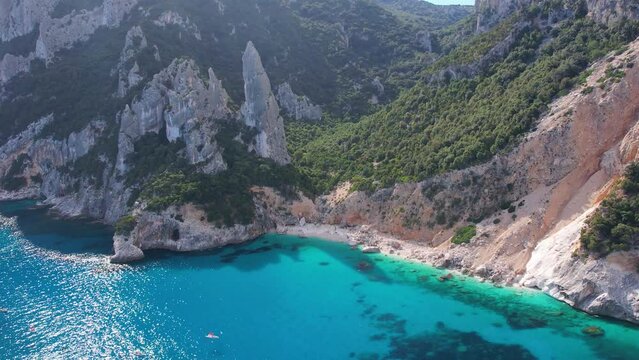 Aerial drone view on white sand Cala Goloritze in Orosei Gulf of Sardegna. Warm turquoise sea, small beach and boats with green mountains on the Sardinia island.
