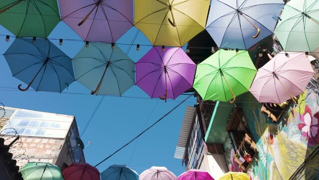Walking under colorful umbrellas above the streets of La Candelaria, sunny Bogota