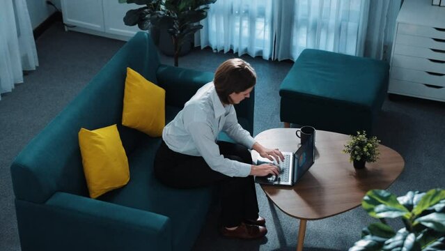 Top view of professional businesswoman working at laptop while lie on sofa. Caucasian project manager using computer to communicate while report sales and relax on sofa. Remote work. Directorate.
