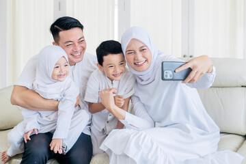 Happy muslim family making a video call or taking a selfie while sitting together on the couch...