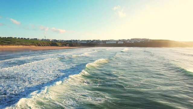 Fistral Beach Surf with Waves Rolling Over Beach. Aerial Drone Tracking Shot with Warm Sunlight.