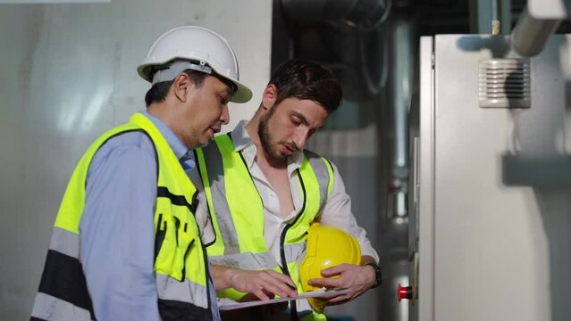 Professional male electrical engineer in safety uniform working and discussion at factory site control room. Industrial technician worker maintenance power system at manufacturing industry plant room.