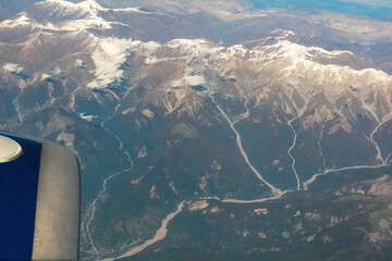 Shot of snowy mountains with mountain rivers descending over them from window of a passenger plane...