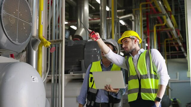 Two professional electrical engineer in safety uniform working together at factory site control room. Industrial technician worker maintenance power system at manufacturing industry plant room.