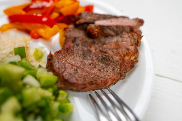 Meal. Beef ribeye steak grilled on charcoal. Fajita, sweet bell peppers, onions, green salsa tomatillo and Basmati rice. Cooked meat and vegetables. Healthy dinner. Plate on white natural wooden table