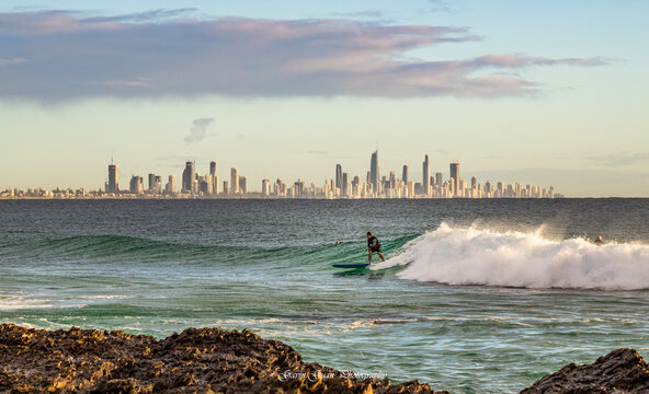 The view of a surfer riding on tide in Burleigh Head with the urban skyline of  Gold Coast in the distance