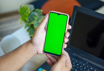 Close-up photo of a man's hand holding a cell phone with a blank green screen