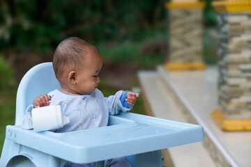 portrait of a cute and adorable Asian baby girl eating while sitting in a baby feeding chair