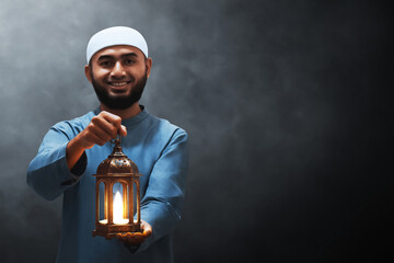 Portrait of handsome young asian muslim man with beard holding arabic lantern and smiling isolated on dark background - 739687812