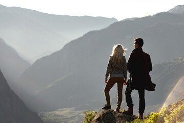 Obraz premium Two young tourists silhouettes stands and look at sunset valley