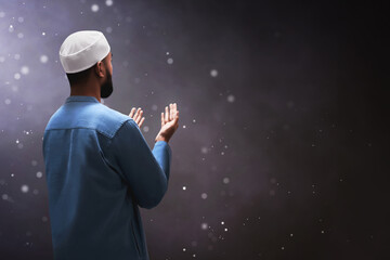 Back view of young asian muslim man with beard praying on dark background - 739688473