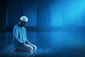 Young asian muslim man with beard praying in the mosque window arch at dark night - 739689003