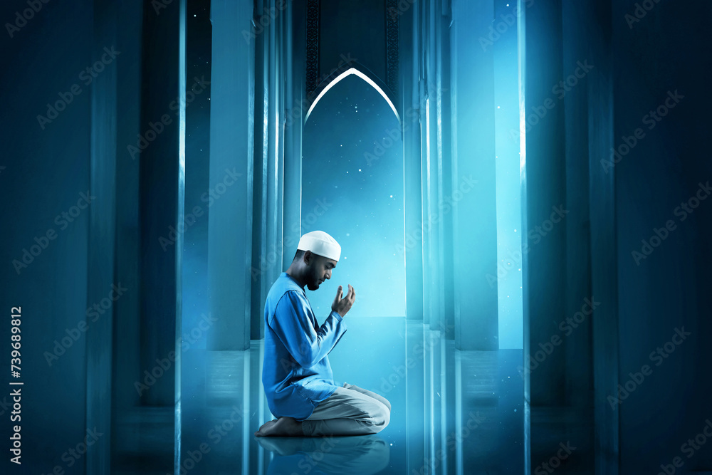 Wall mural Young asian muslim man with beard praying in the mosque door arch at beautiful blue night sky with stars