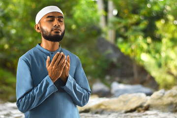 Portrait of handsome young asian muslim man with beard praise, thankful and relaxing in forest with green trees