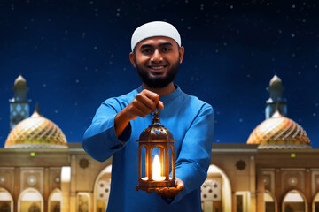 Portrait of handsome young asian muslim man with beard holding arabic lantern and smiling at beautiful blue night sky with star - 739691669