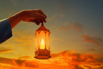 Hands of young asian muslim man holding shiny arabic lantern at beautiful sunset sky with cloud - 739693077