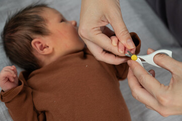 Obraz na płótnie Canvas Mom cuts her newborn son's fingernails with small children's scissors.
