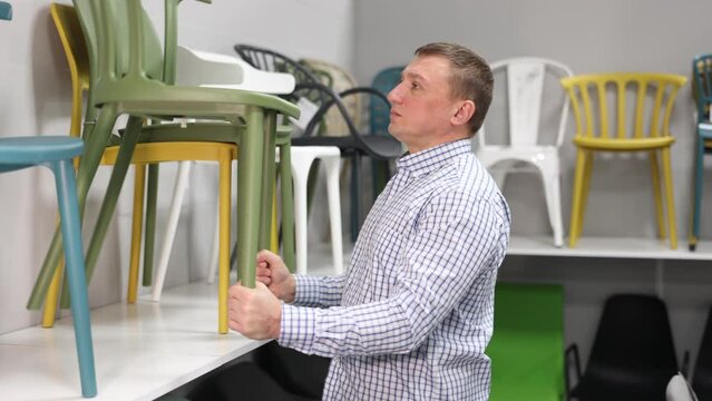 Focused adult man looking for new practical chairs for his apartment in furniture store, carefully examining displayed samples