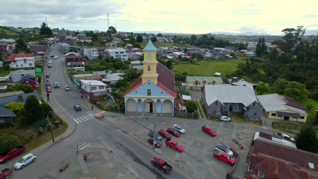 Aerial orbit establishing the heritage church of Chonchi in Chiloe, Chile with a sunny horizon with clouds.