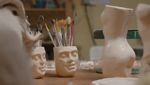No people shot of various size paint brushes and artist tools in handmade ceramic face holder on desk in small creative sculpting workshop