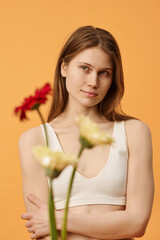 Selective focus studio portrait of young Caucasian woman wearing comfortable bra standing against warm apricot wall background looking away
