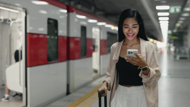 Charming Woman Getting Off the Train with Luggage and Looks at Map on the Phone. Young Tourist Got Out of the Subway Wagon with Suitcase and Looking Information on the Internet. Travel and Technology.