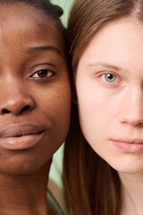 Vertical close-up studio shot of faces of two young African American and Caucasian women with no makeup posing for camera cheek to cheek