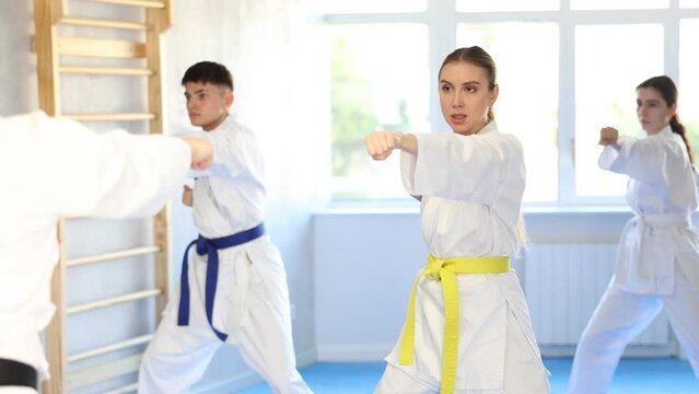 Diligent young woman attendee of karate classes practicing kata standing in row with others in sports hall