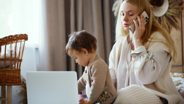 Pretty young single mom working at home on a laptop computer while holding her baby girl 