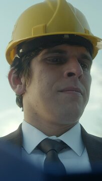 Vertical video. A Young, Beardless Construction Engineer or Contractor in a Helmet and Suit Examining Blueprints in a Blue Folder and Getting Frustrated over a Faulty Detail	