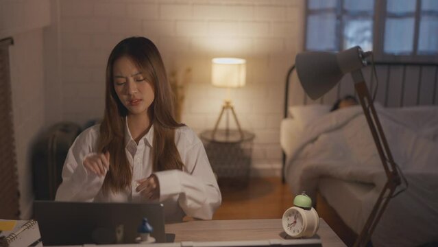 Depressed Asian young woman overworking while husband sleeping at night. 