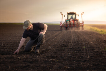 Farmer examing dirt while tractor is sowing field