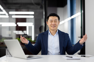 Naklejka premium Portrait of smiling and resting young man, Asian businessman taking a work break, sitting relaxed in lotus position at table with closed eyes.