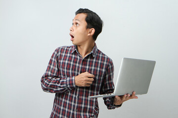 Shocked and wow expression of asian indonesian man holding laptop computer on isolated background