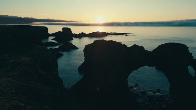 Incredible drone aerial of coral sea arch and coastal lands during sunset.  Gatklettur.  Hellnar Arch Iceland.  The camera moves from right to left.