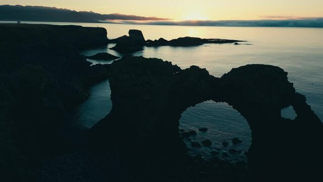 Incredible drone aerial of coral sea arch and coastal lands during sunset.  Gatklettur.  Hellnar Arch Iceland.  The camera moves from right to left.