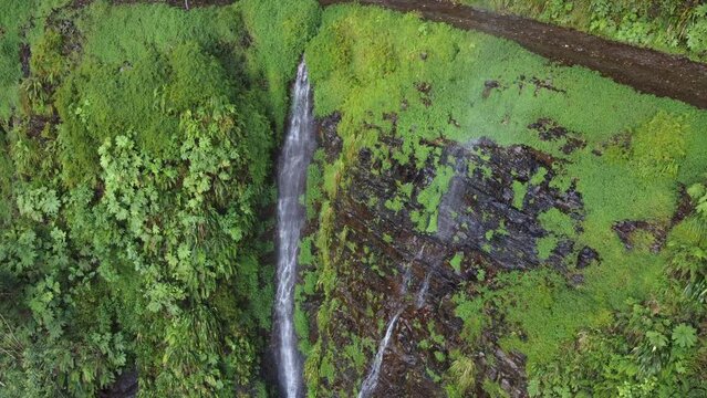 Steep cliff waterfall flows onto narrow mountain dirt road in Bolivia