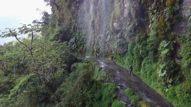 Aerial through waterfall following cyclists on Bolivia's Yungas Rd
