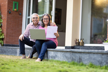 Senior couple using laptop together at home backyard