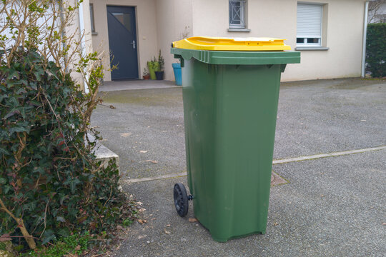 Recycling bin green trash can with yellow lid for sorting recyclable packaging in front of the house waiting for the garbage collectors to pass stands outdoor