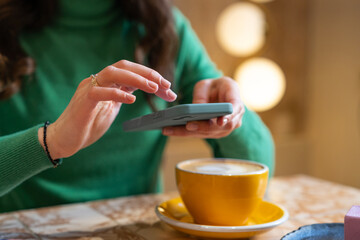 Blogger using mobile phone in the coffee shop. Woman reading good news on mobile phone during rest in coffee shop