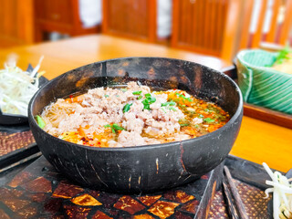 Spicy tom yum noodles with minced pork in wooden bowl. Thai street food concept. ....