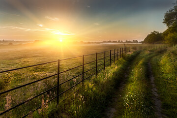 Castle Rising, In Norfolk England. Super sunrise over farm fields cattle fence and track - obrazy, fototapety, plakaty