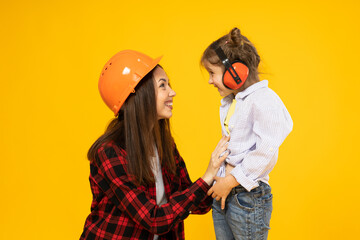 Mother and daughter in accessories for construction, on a yellow background. - obrazy, fototapety, plakaty